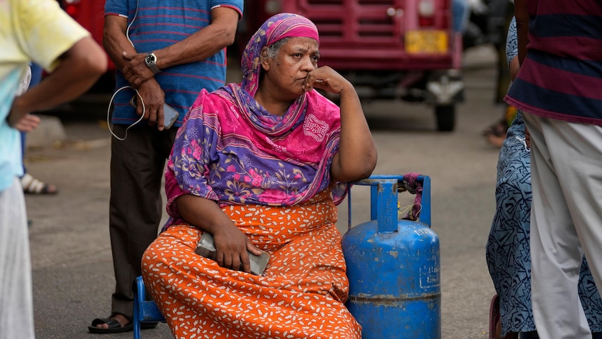 A woman sits on the ground, head in her hand.