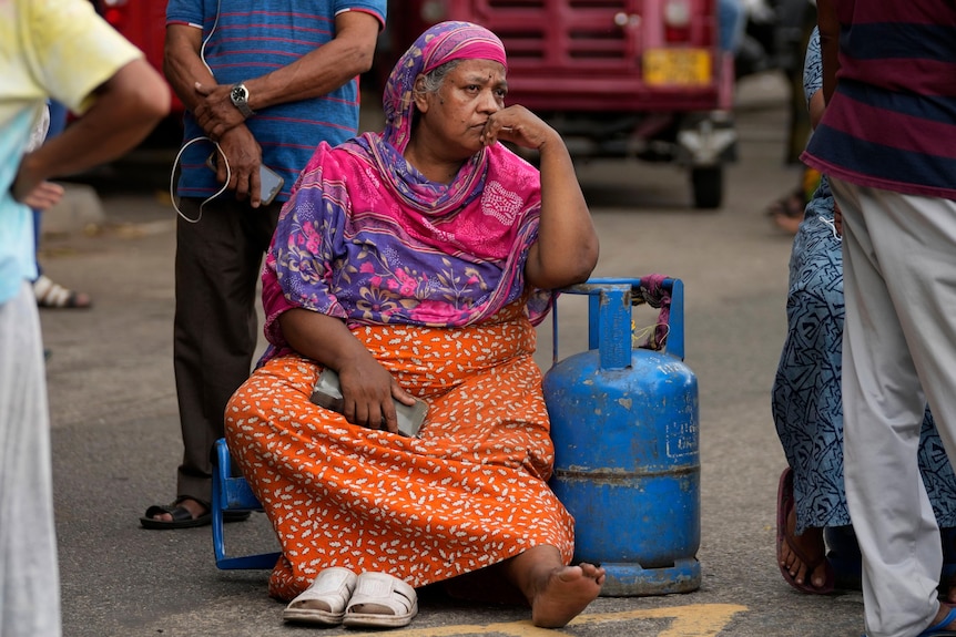 O femeie în vârstă care stă pe stradă ținând o sticlă de gaz