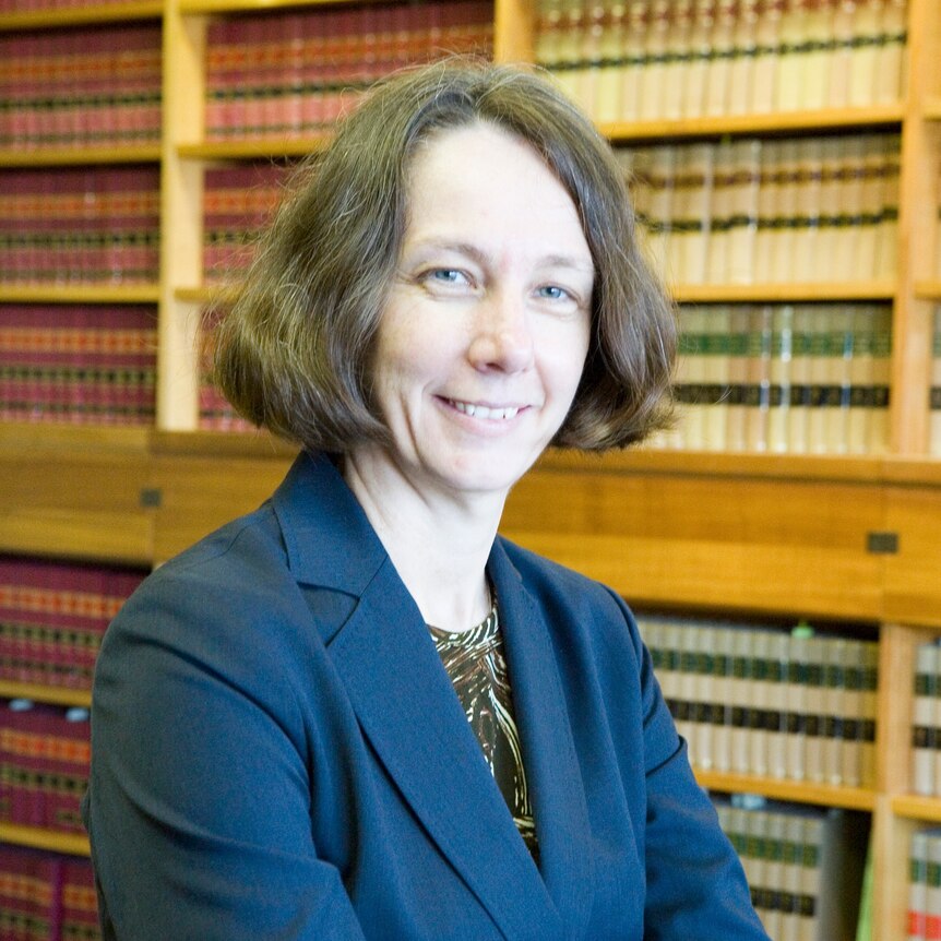 Justice Jayne Jagot wearing a blue blazer smiling with her arms crossed in front of her in front of a bookcase
