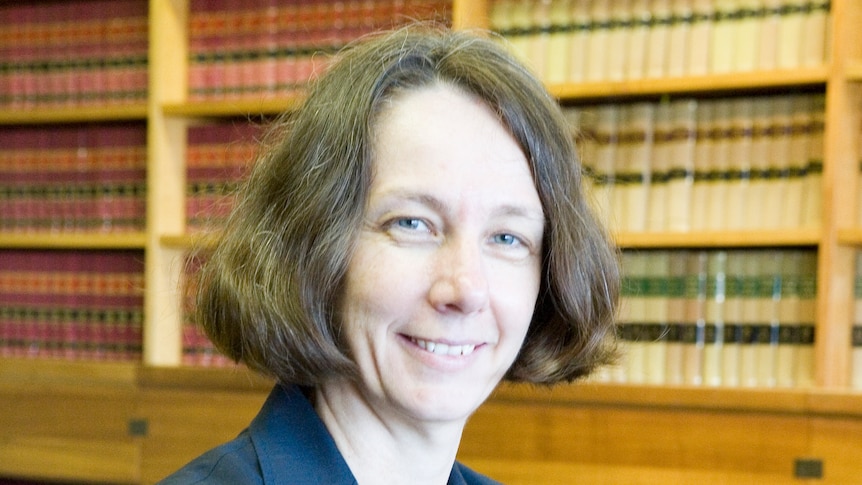 Justice Jayne Jagot wearing a blue blazer smiling with her arms crossed in front of her in front of a bookcase