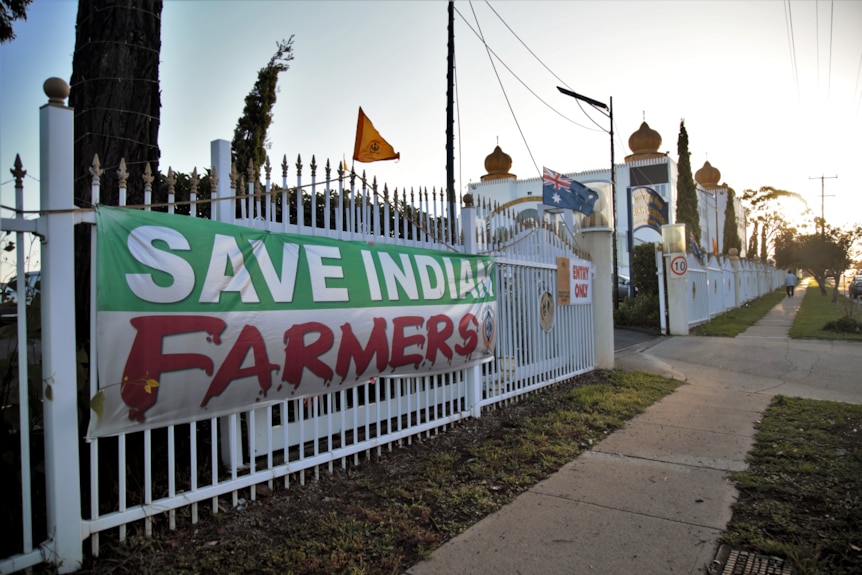 The exterior of a Sikh temple with a sign that says "Save Indian farmers" hung on the fence