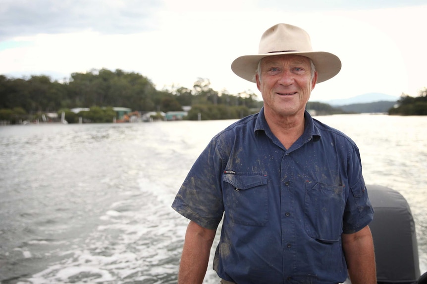 A fisherman wearing an Akubra hat stands on the back of a moving boat.