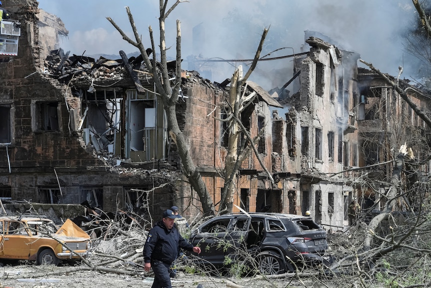 A view of ruined cars and charred buildings with smoke visible.