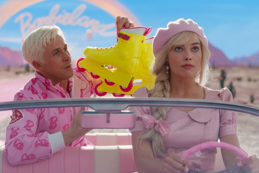 Ryan Gosling as Ken holding fluro yellow roller blades with Margot Robbie as Barbie in the Barbie car