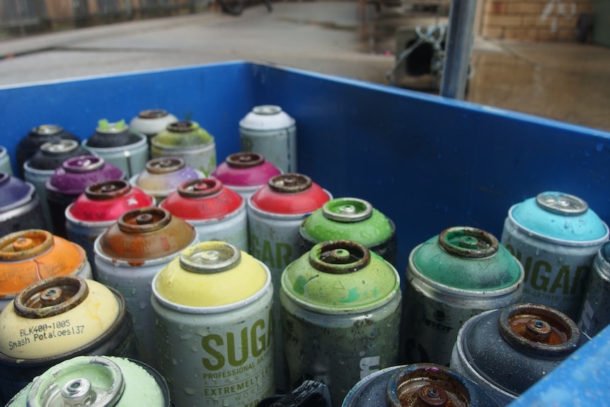 A close-up photo of several cans of spray paint in a blue plastic container.