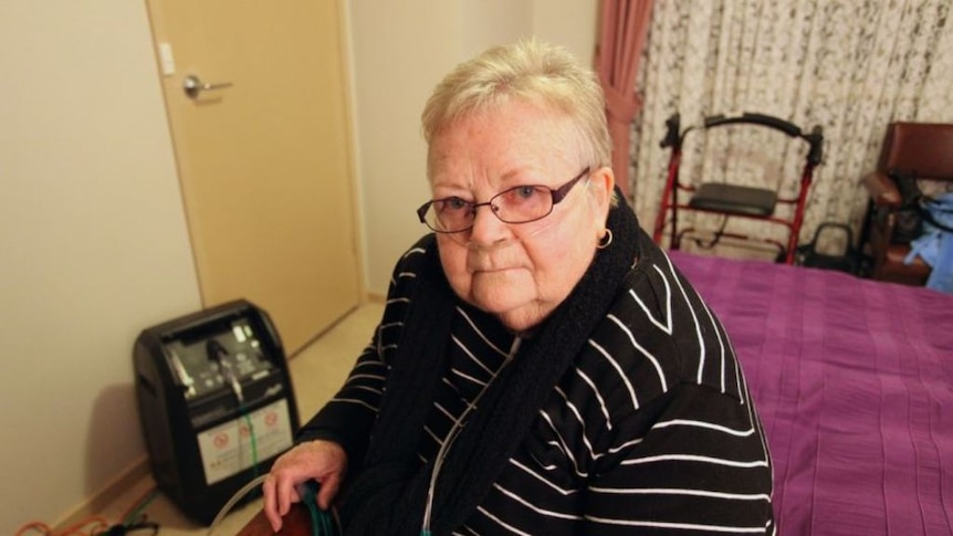 Eileen Kelly, seated on a bed, wears breathing equipment.