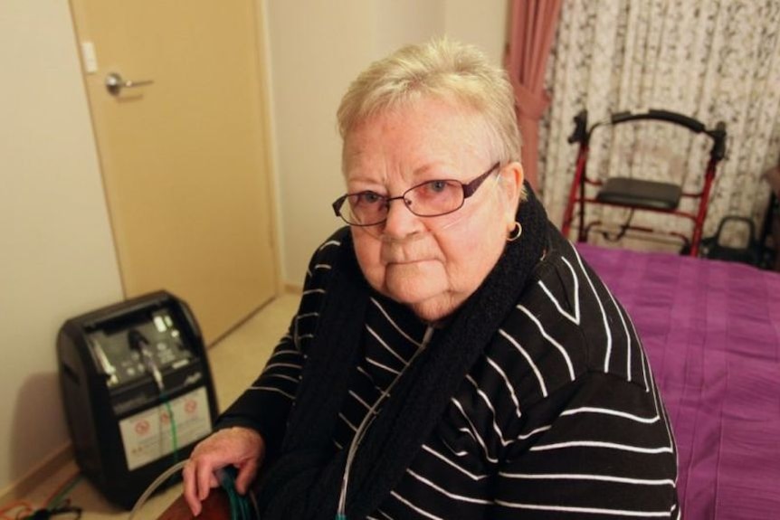 Eileen Kelly, seated on a bed, wears breathing equipment.