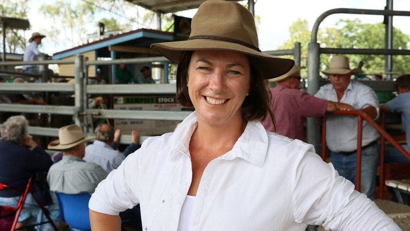 A woman with her hands on her hips, wearing a hat and a white shirt, smiling.