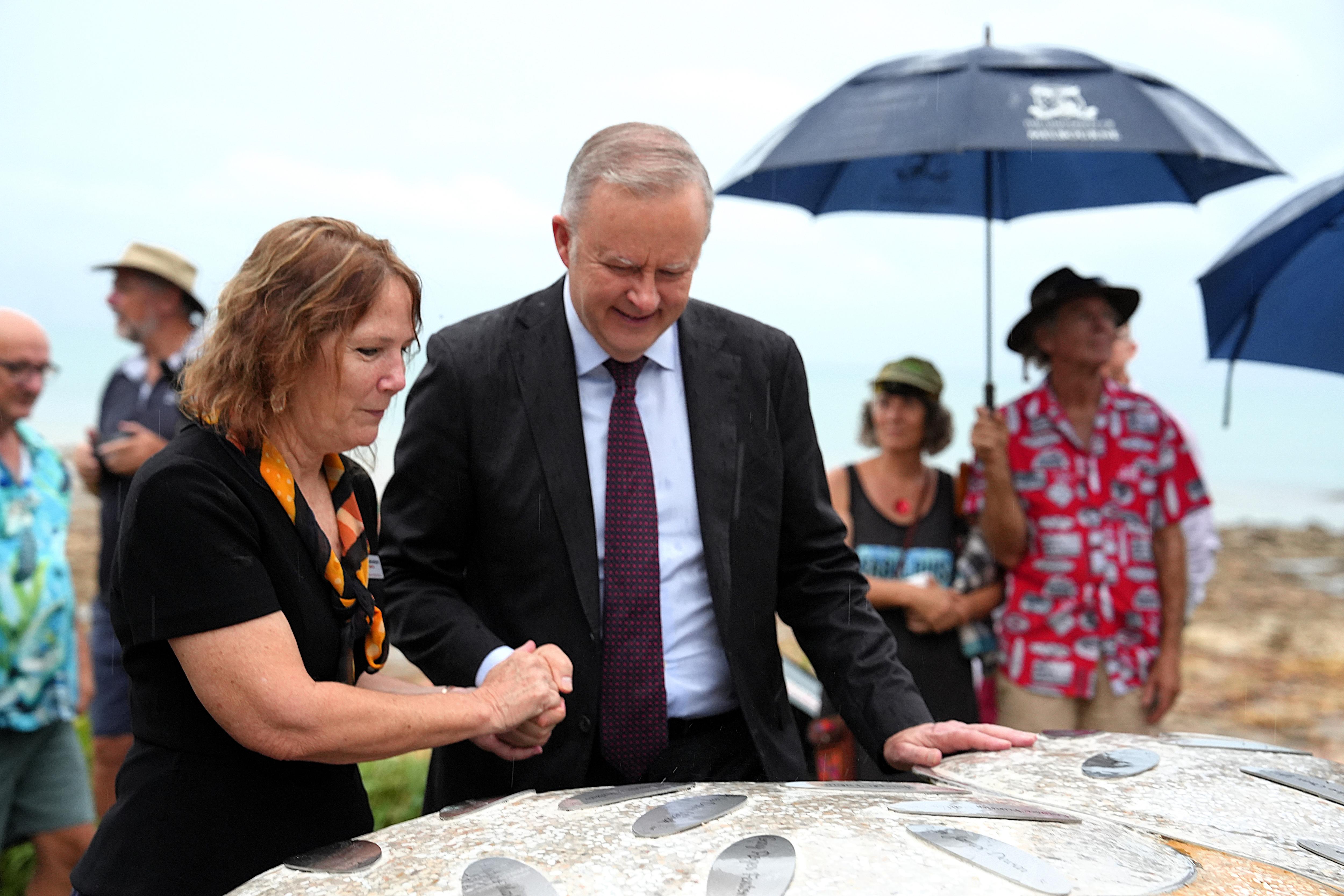 A man and woman hold hands as they stand beside a memorial.