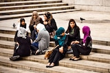 Group of young women wearing hijabs and sitting on stairs.