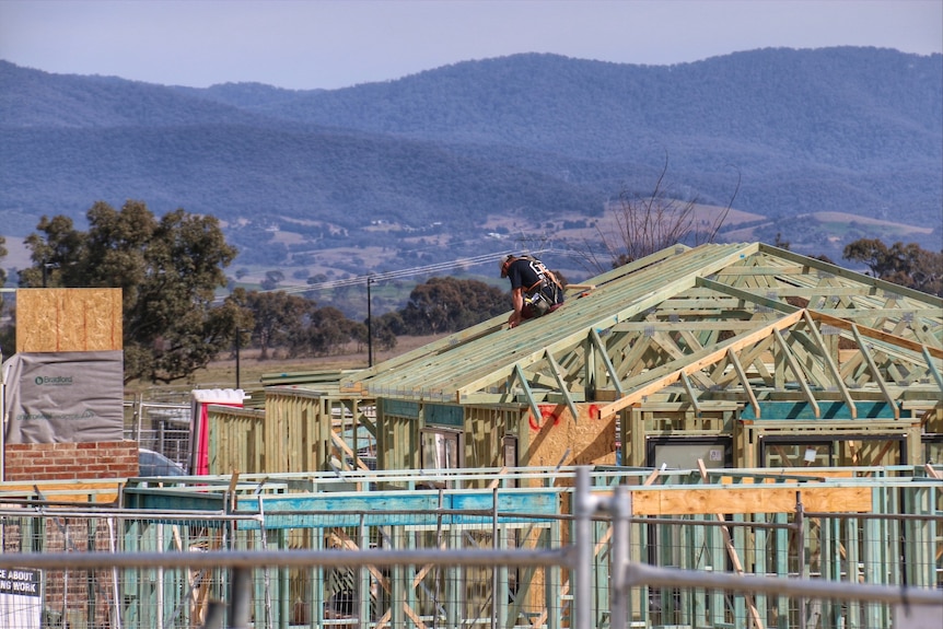 A construction worker sits atop a house frame.