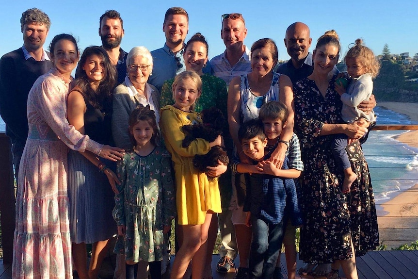 A big multi-generational family stands on a deck over looking a beach