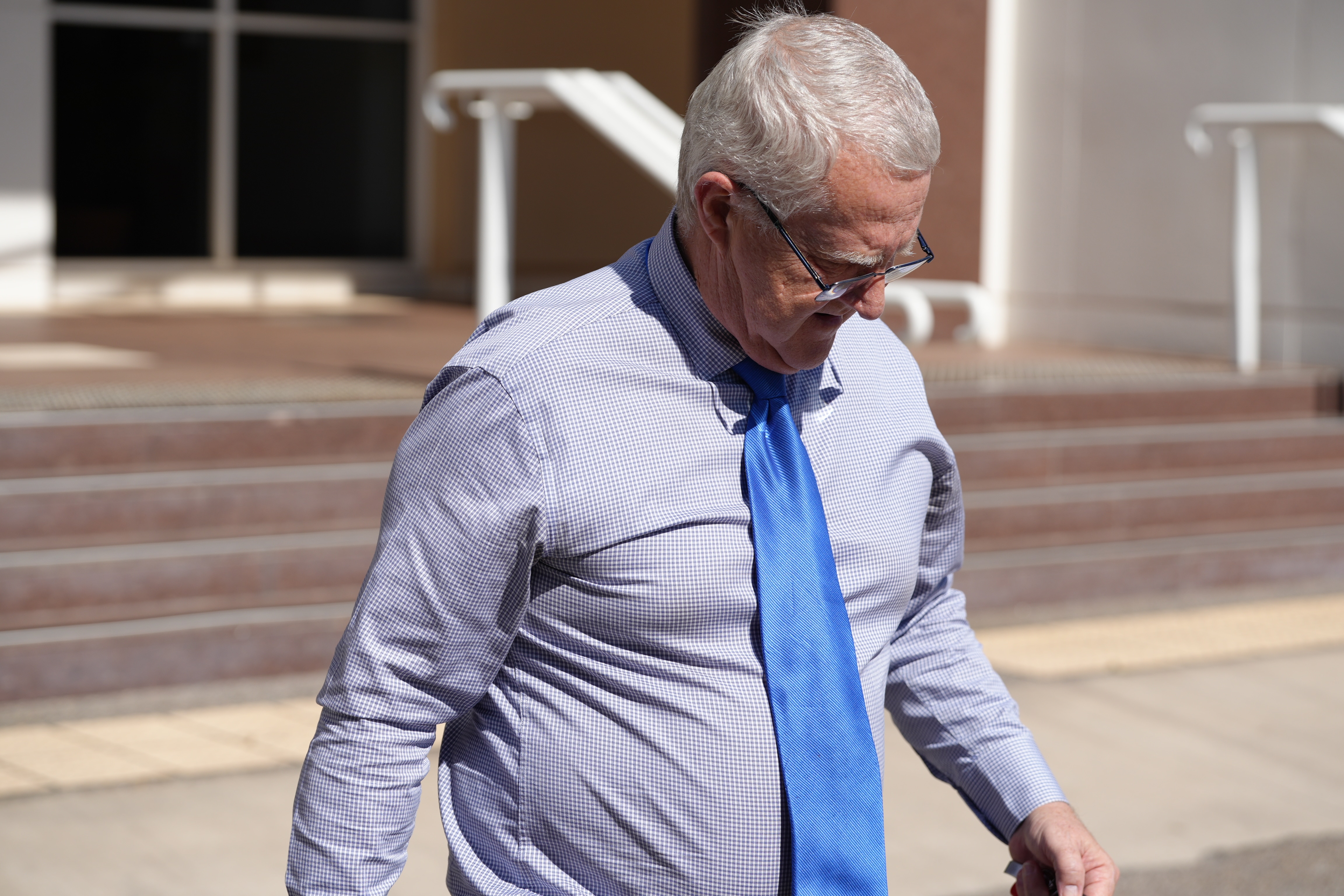 A man in shirtsleeves and a blue tie leaves court.