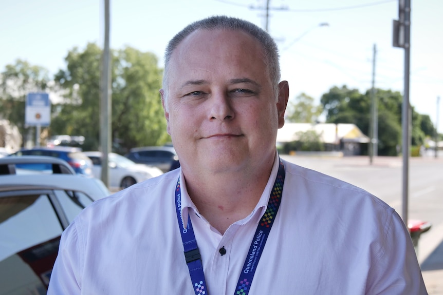 A man in a light coloured collared shirt looks at camera