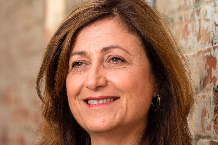 Carmel Guerra, a woman with light brown hair, smiling against a wall.