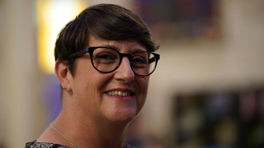 Woman with short hair and black-framed glasses smiling. 