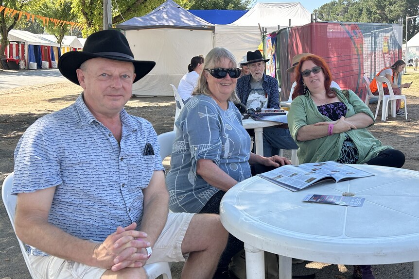 Three people sit at an outdoor table at a festival.