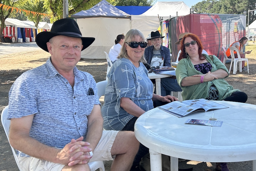 Three people sit at an outdoor table at a festival.