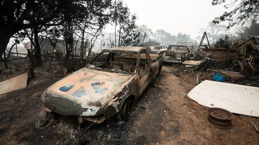 Scorched cars are seen in the aftermath of the Wingello fire as smoke shrouds the skyline.