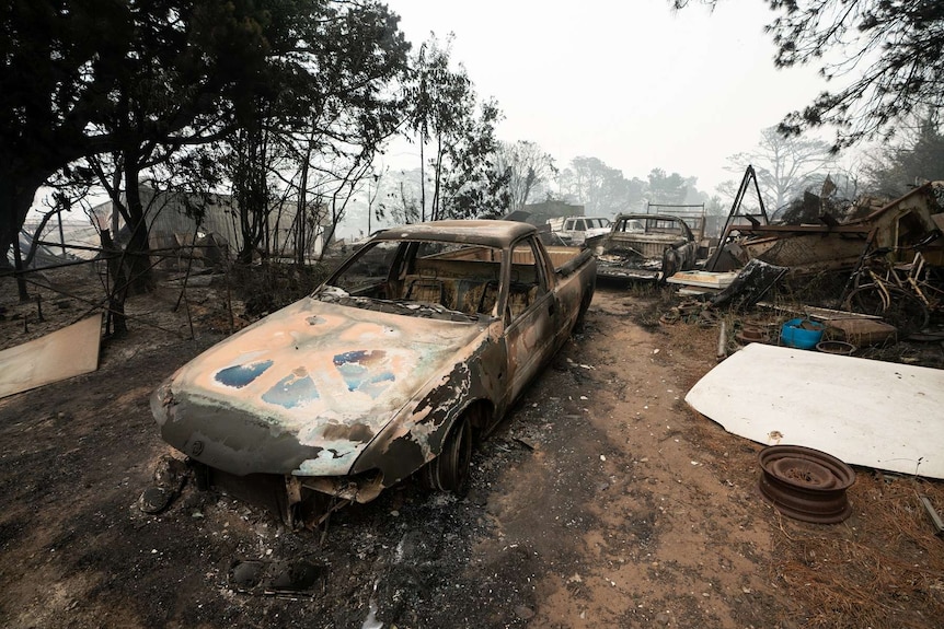 Scorched cars are seen in the aftermath of the Wingello fire as smoke shrouds the skyline.