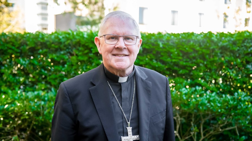 Archbishop Mark Coleridge in front of green hedge.