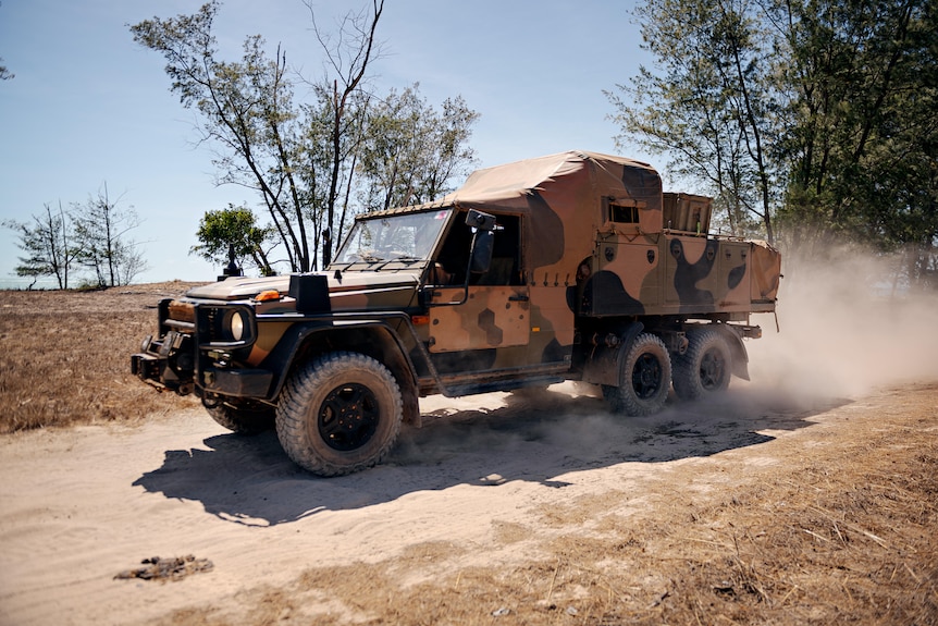 an army vehicle travelling on a sandy road in the sunshine