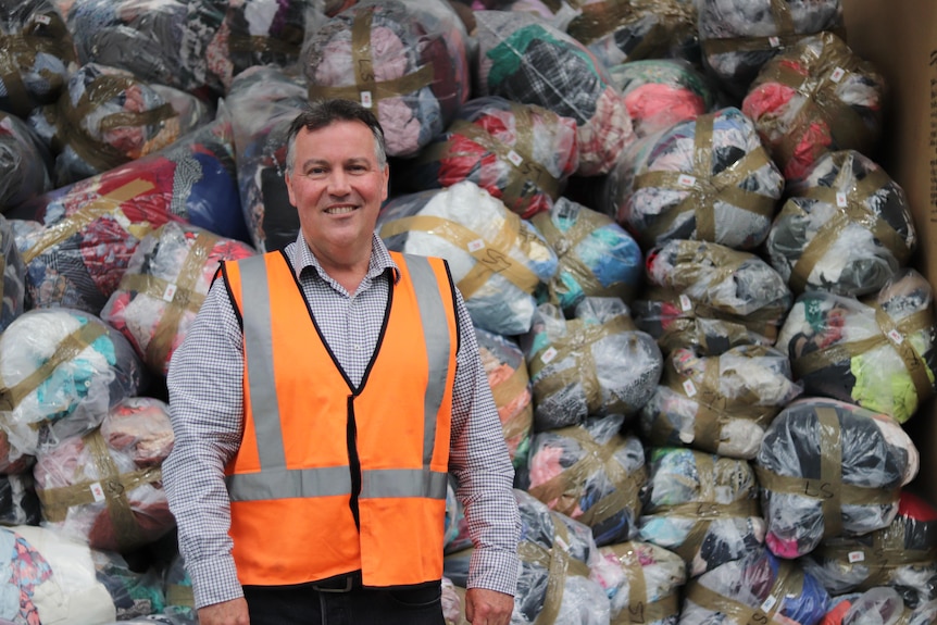 A man wearing a high-vis vest stands in front of a pile of donated clothing.