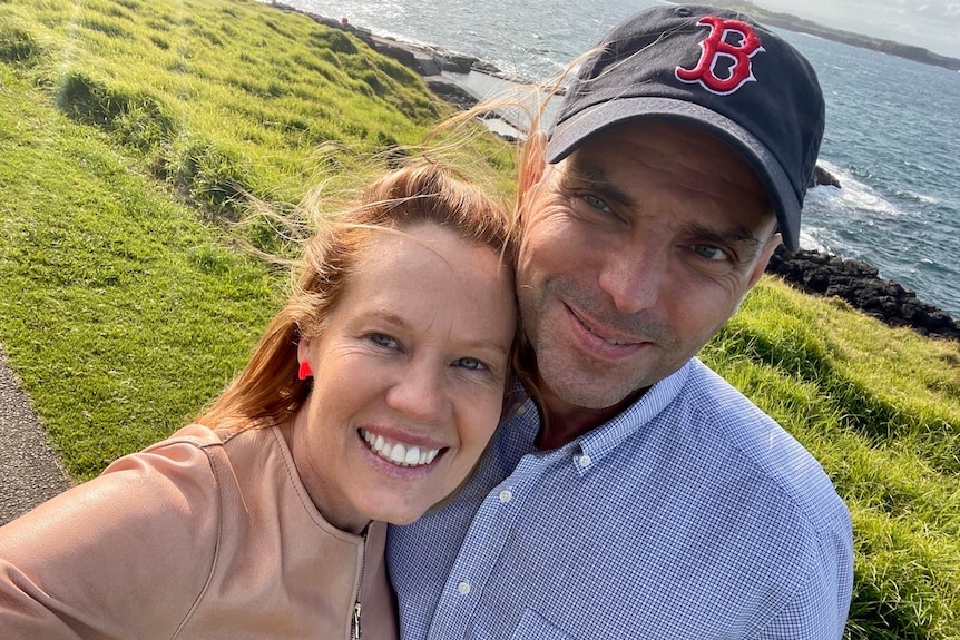 Man and woman in an embrace on a grassy hill near the ocean. 