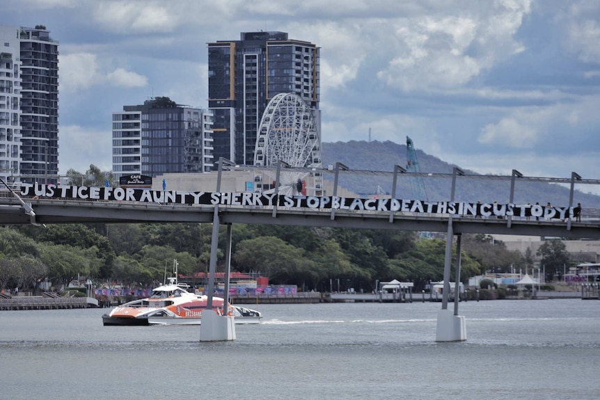 The Brisbane river is seen with a sign on a bridge that says "Justice for Aunty Sherry Stop Black Deaths in Custody".
