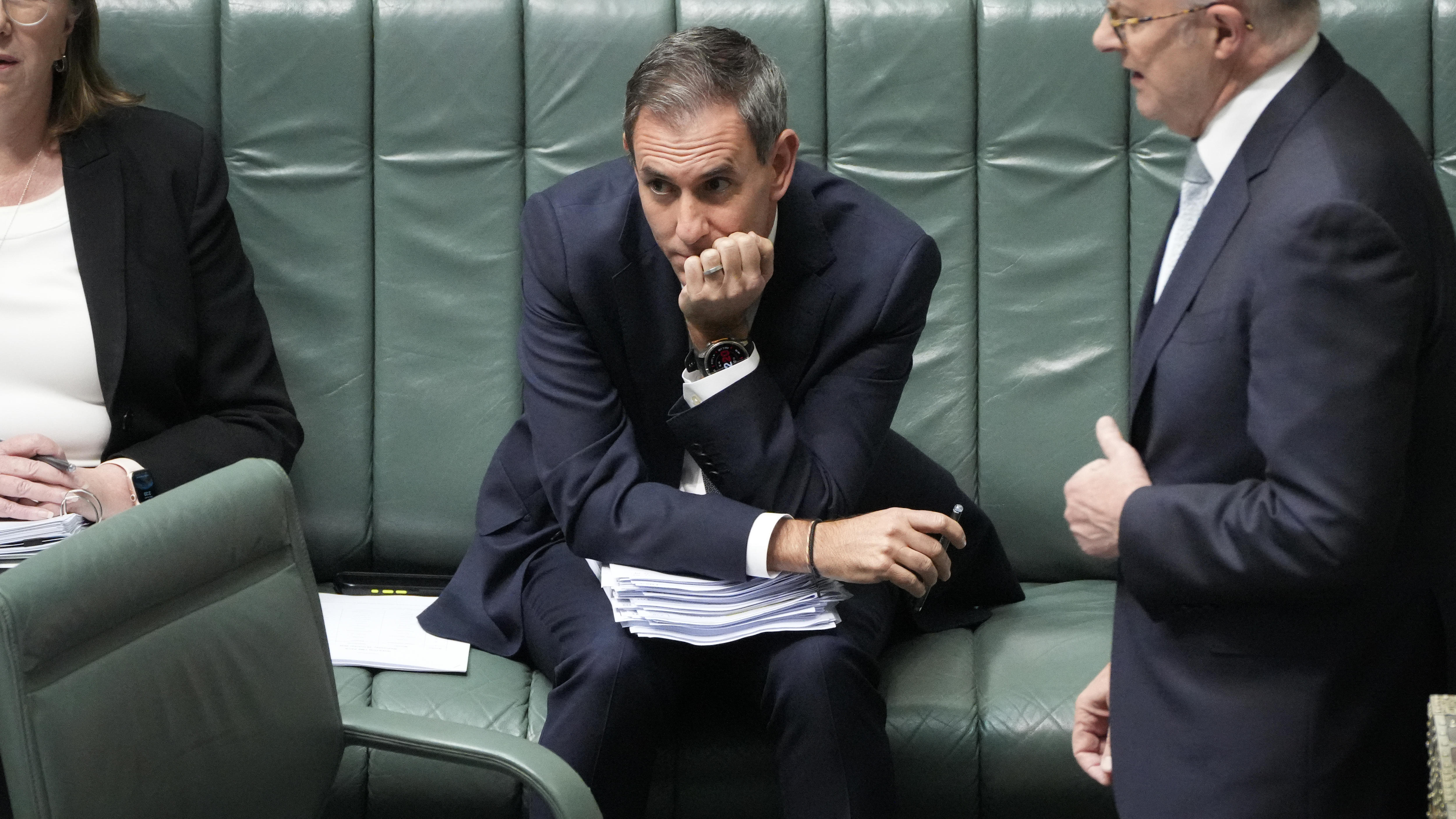 Jim Chalmers sits in parliament with papers on his lap and his chin in one hand, looking sheepish