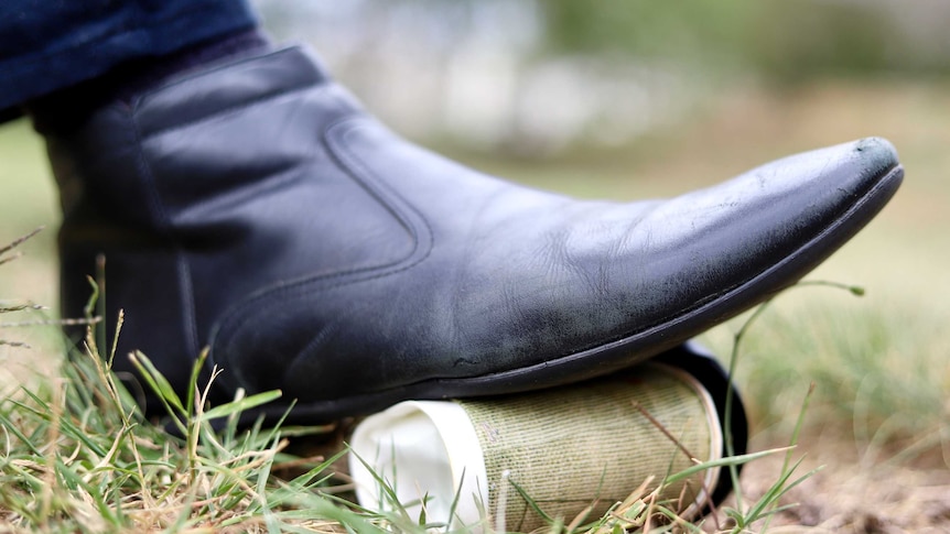 A disposable coffee cup is crushed by a foot.