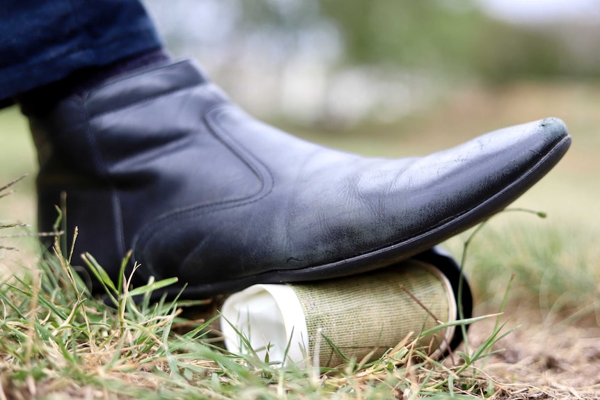 A disposable coffee cup is crushed by a foot.