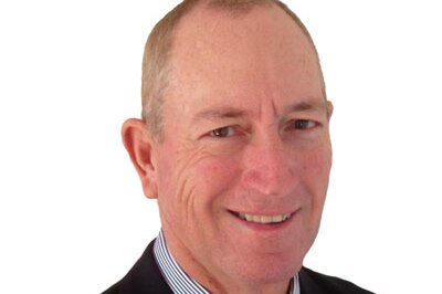 Fraser Anning, photographed against a white background, wearing a black suit and and tie with a striped shirt.