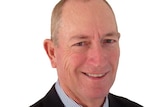 Fraser Anning, photographed against a white background, wearing a black suit and and tie with a striped shirt.