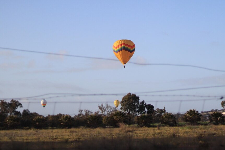 Long distance shot of a yellow hot air balloon flying along.