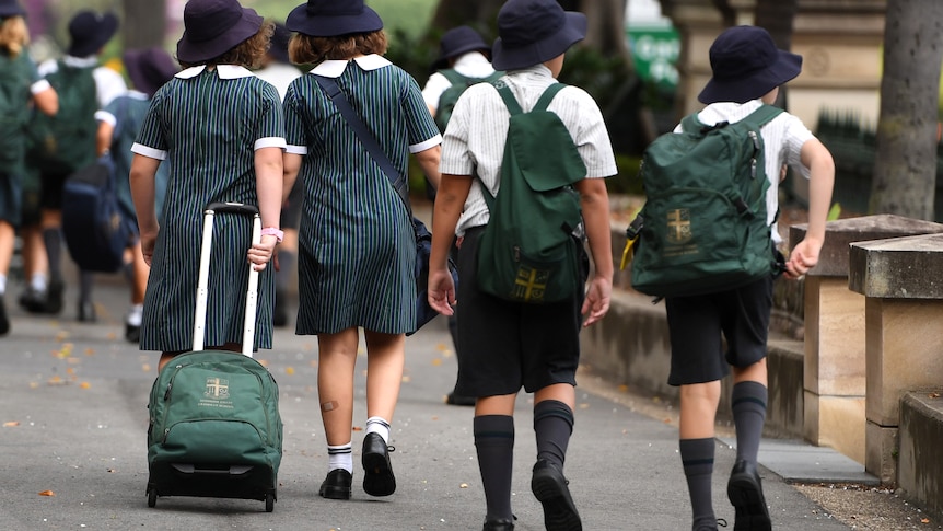 Primary aged school stduents with school logo green backpacks walk along a city street