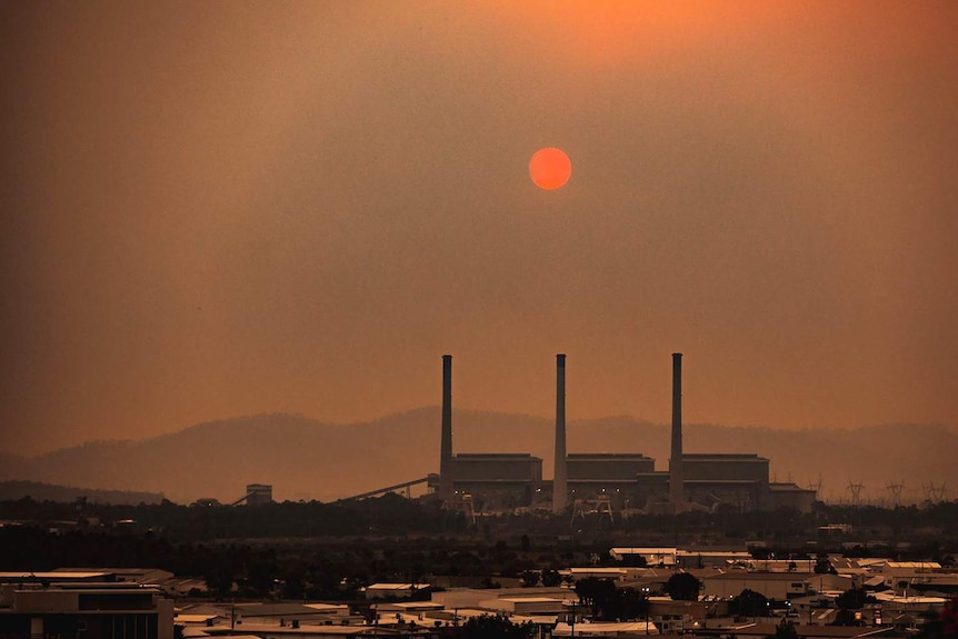 Smoke haze from bushfires with sun in bright red silhouette hangs over Gladstone with aluminium smelter stacks in view.