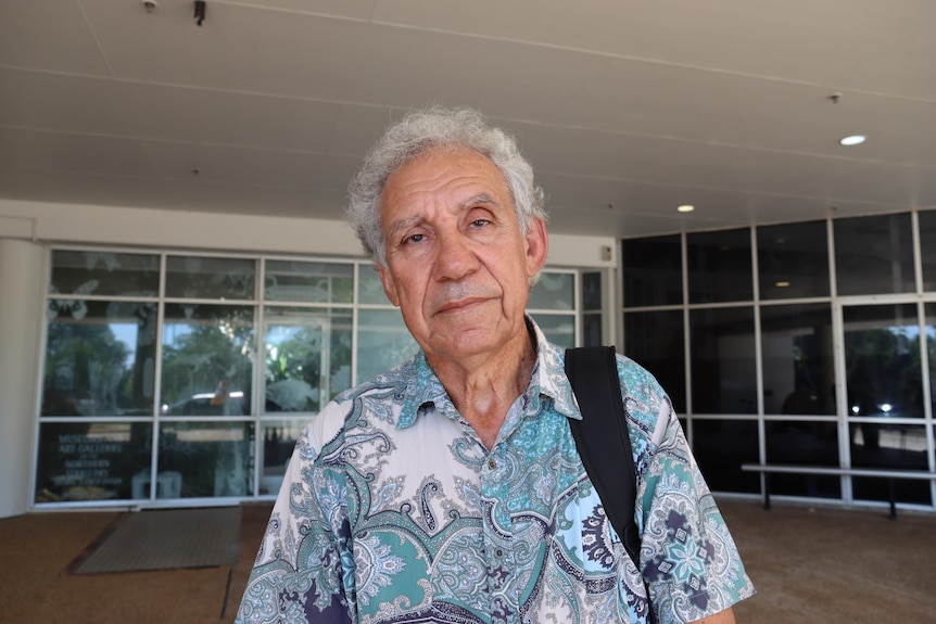 Broadcaster Charlie King standsin front of a building. He has a neutral expression