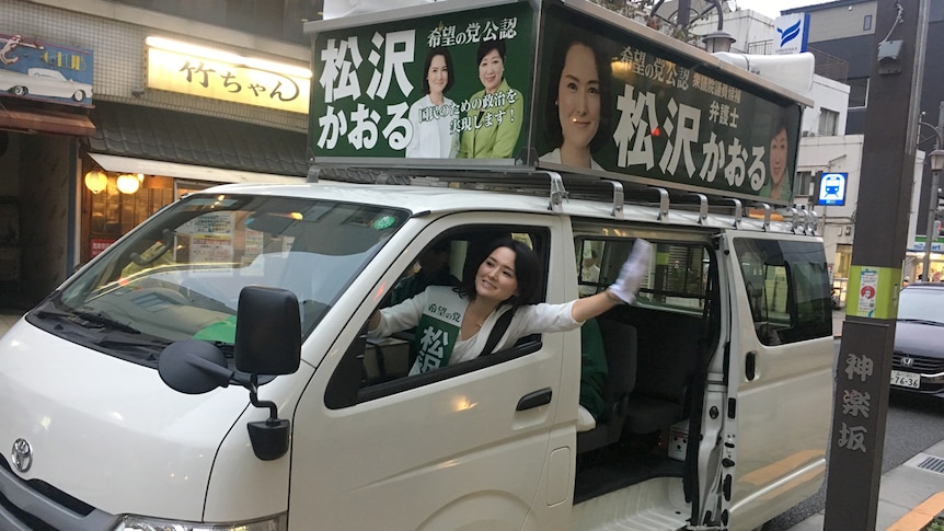 A woman smiles and waves through the window of a van wearing white gloves.