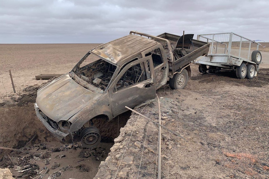 A burnt ute with a trailer attached crashed in a bare paddock