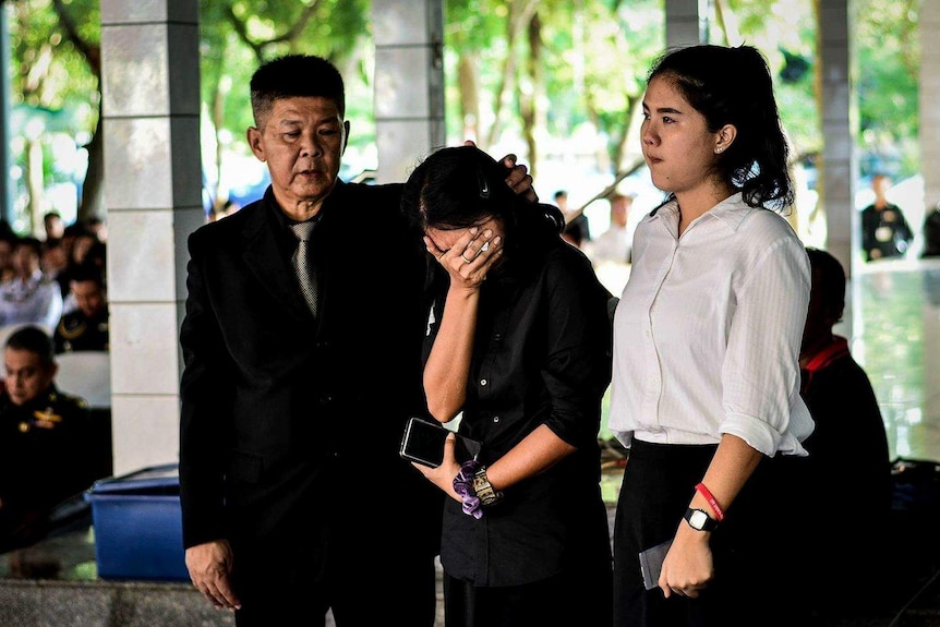 A man comforts his crying wife and stands with their daughter.