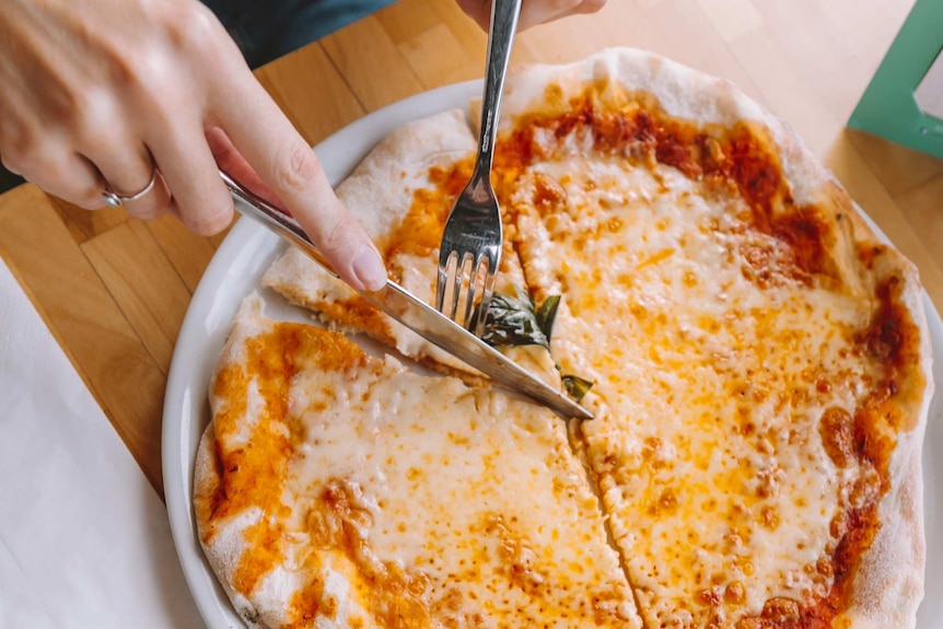 A woman cuts into a thin pizza topped with tomato sauce and cheese, for a fast meal.