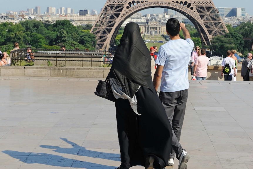 A woman walks near the Eiffel Tower wearing a burka.