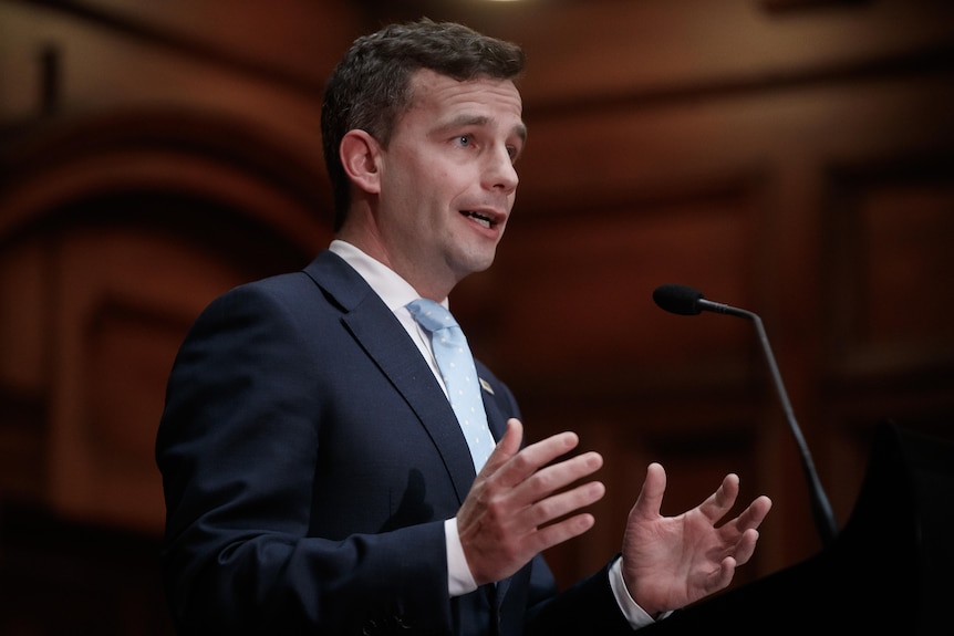 A man wearing a suit speaks into a microphone. 