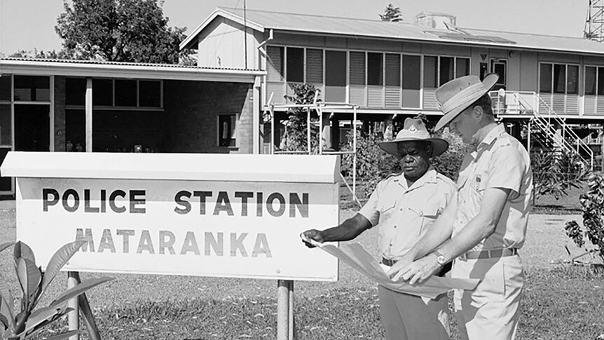 An archival photo of two policemen inspecting a map outside the Mataranka police station.