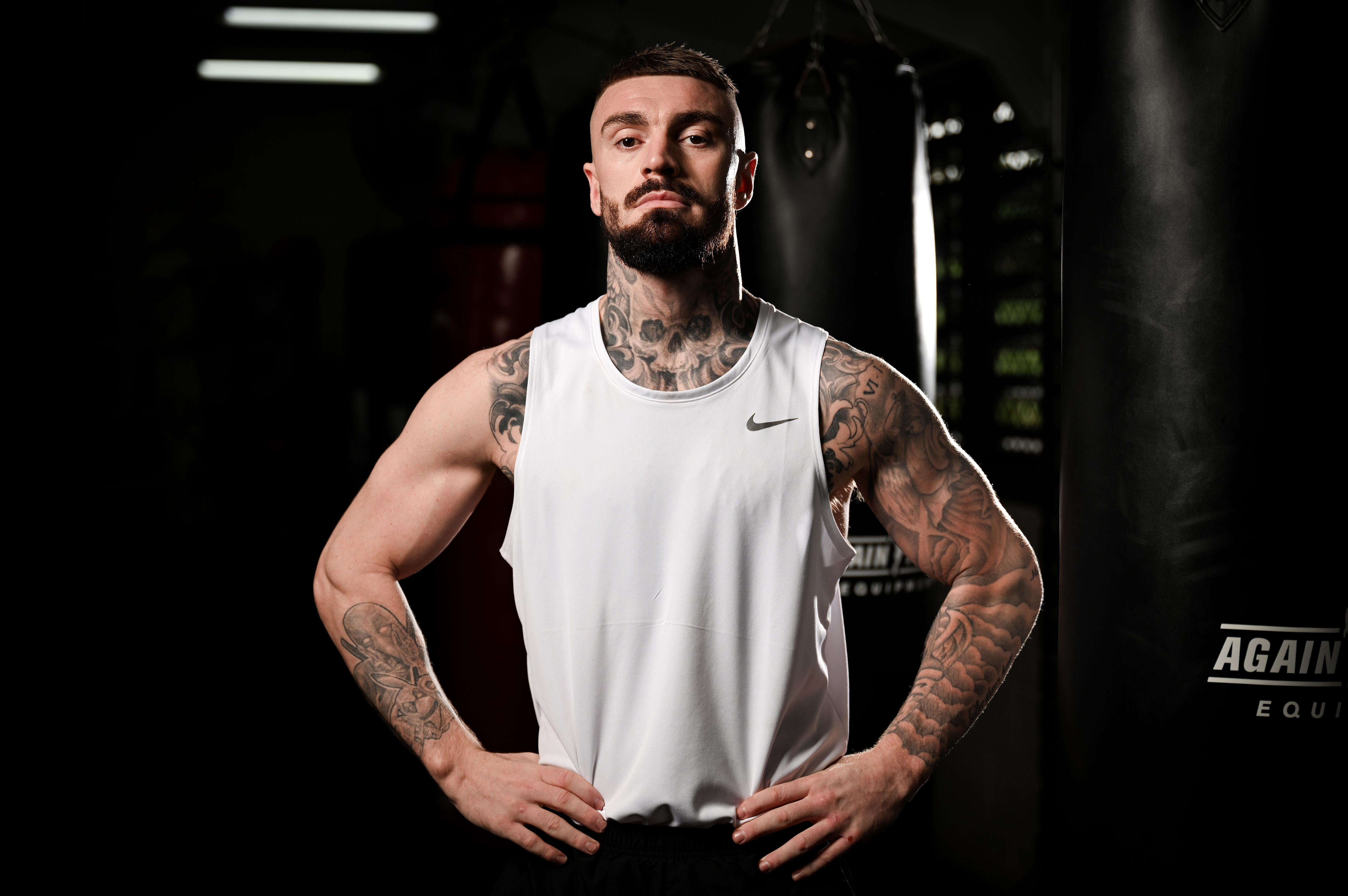 Boxer Lewis Crocker ikn a white singlet, in a gym, posing with hands on hips