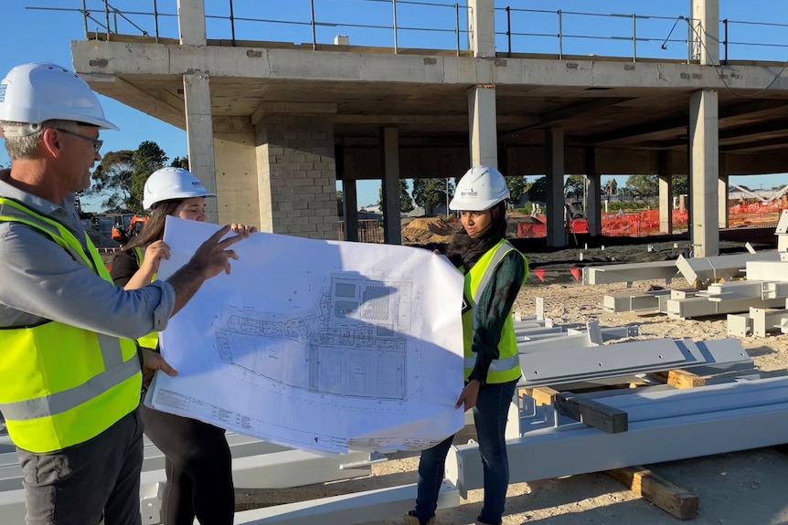 Man looks at plans held by two women on construction site