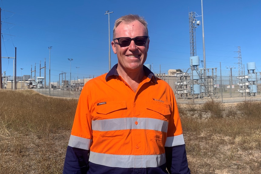 a man in high vis and sunnies stands in front of a substation.