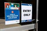 Two signs on a door that say "COVID-19 vaccination location" and "entry only".