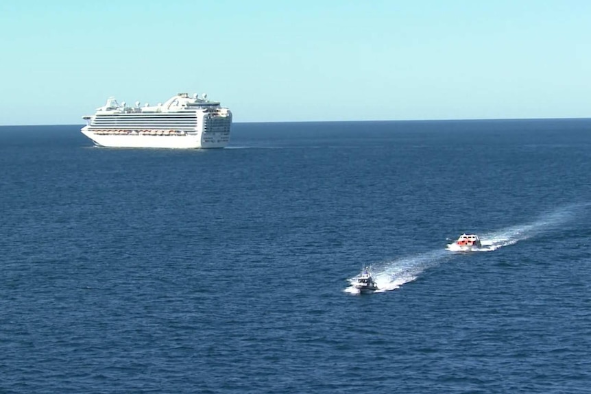 Two much smaller boats move across the water away from a large cruise ship.